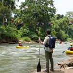 Dandeli adventure scene featuring travelers preparing for river rafting on Kali River amidst lush greenery.